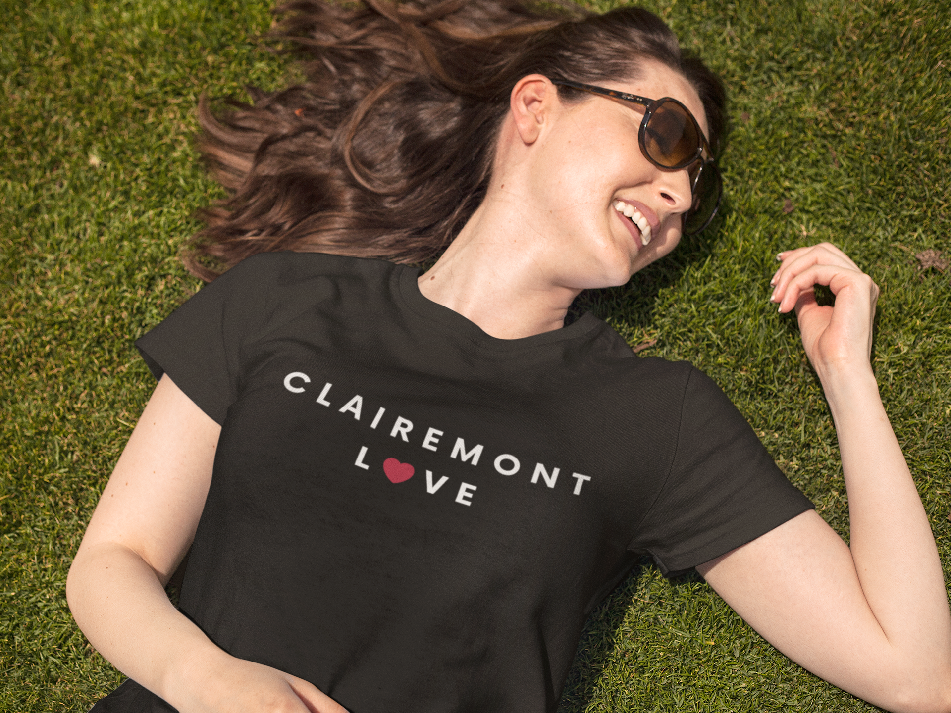 Woman with sunglasses laying in the grass wearing a Clairemont t-shirt.