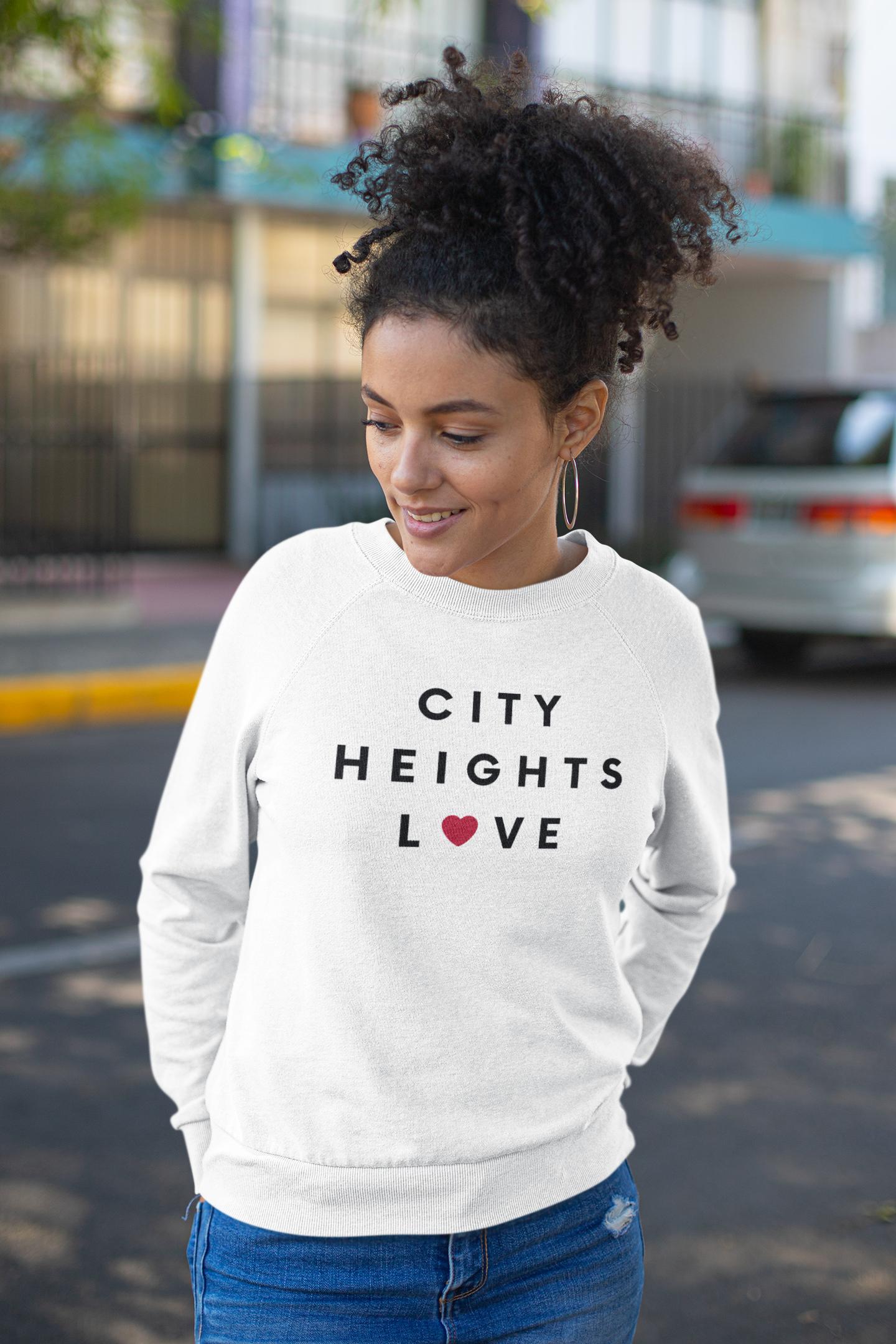 Curly haired women standing outside a building wearing a City Heights sweatshirt.