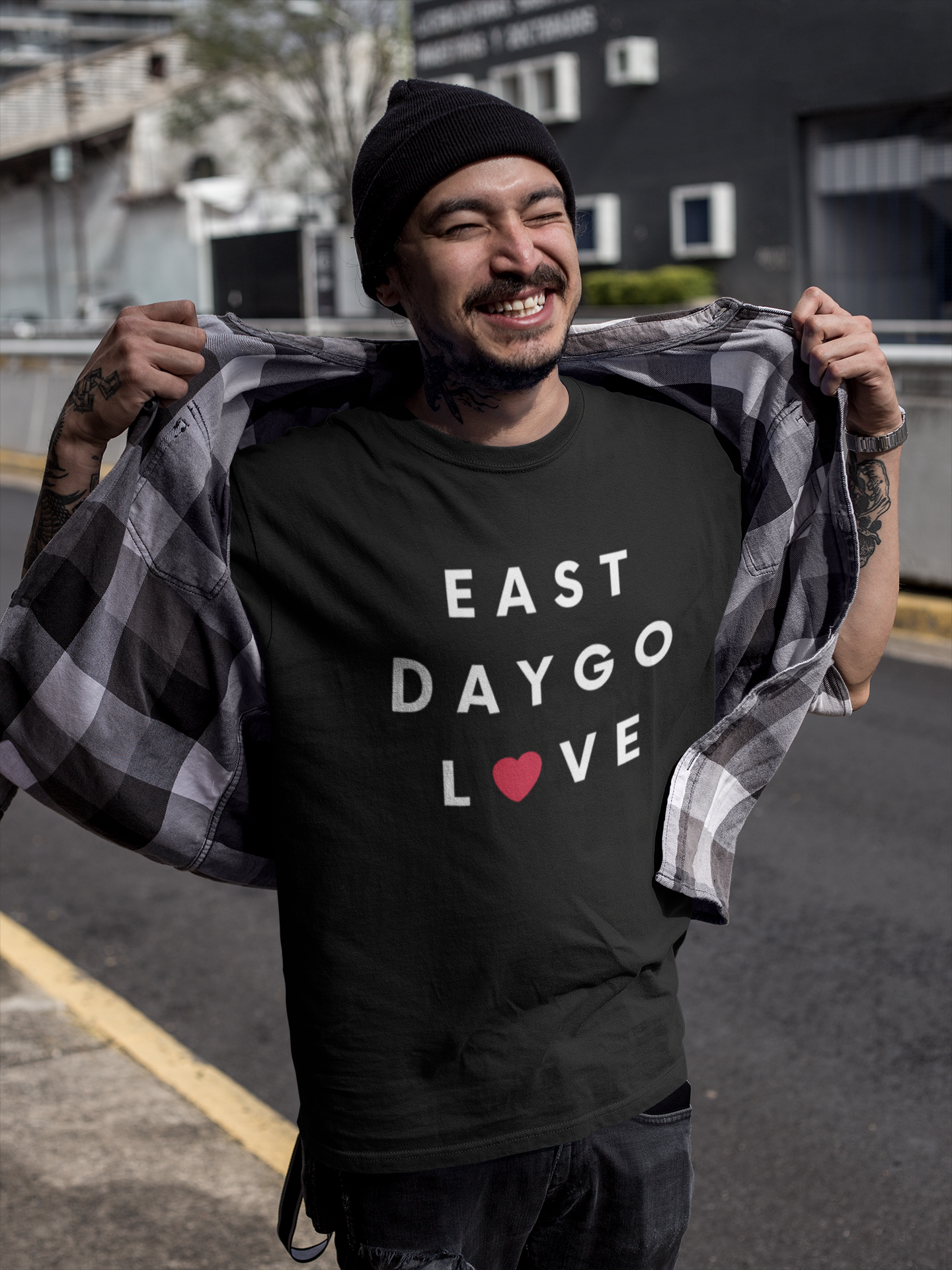 Smiling Asian man with tattoos standing outside buildings wearing a beanie and East Daygo t-shirt. 