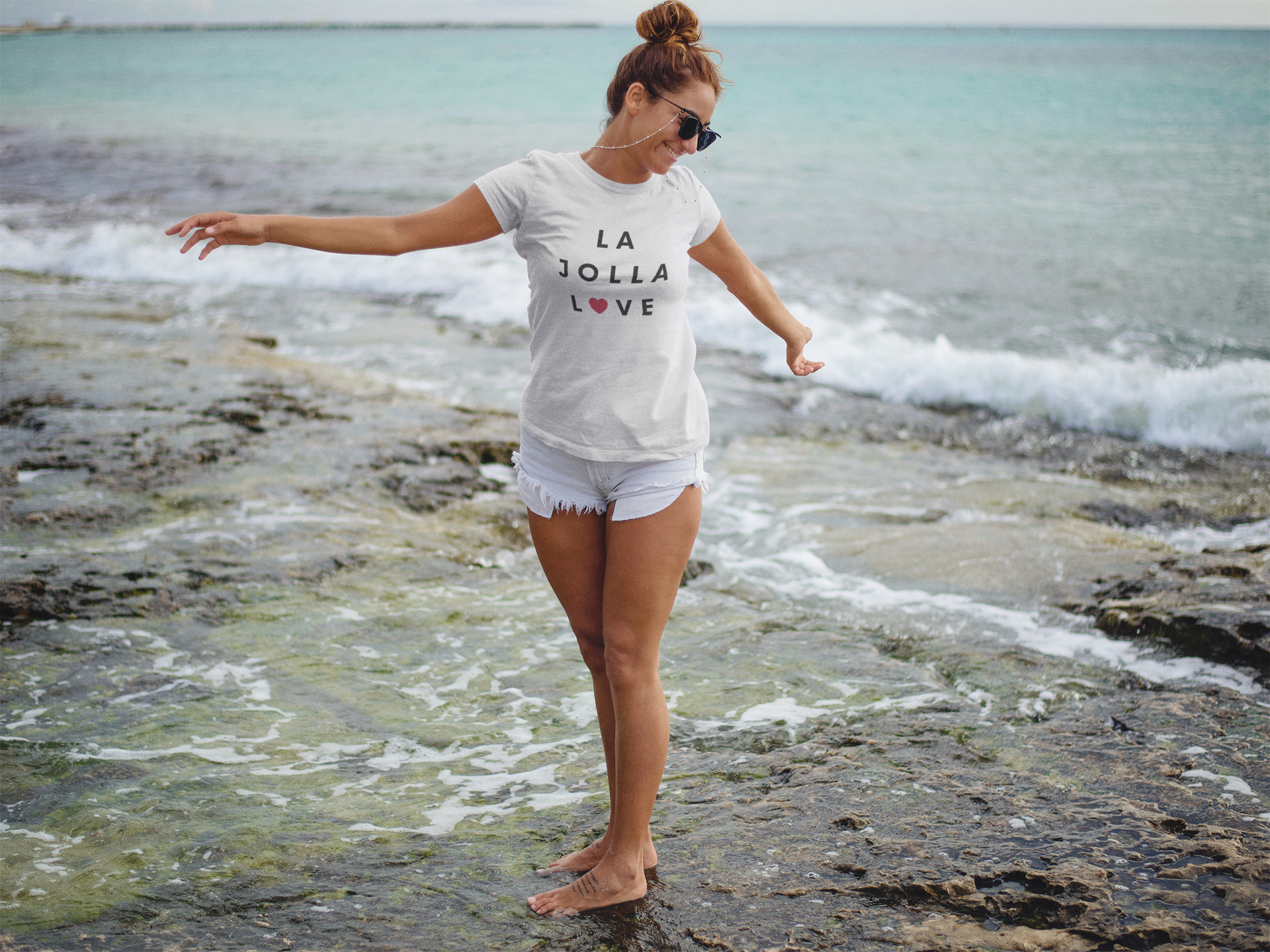 Trendy woman with sunglasses standing in ocean wearing a La Jolla love t-shirt.