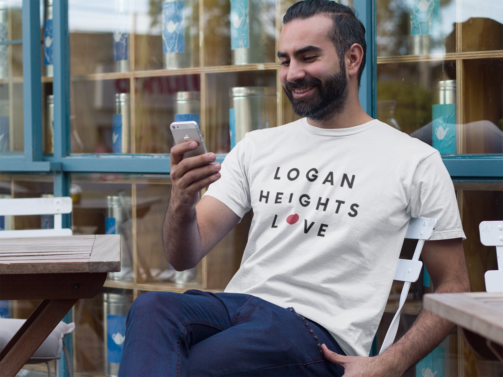 Hispanic man sitting outside smiling while looking at his phone. Man wearing Logan Heights t-shirt.