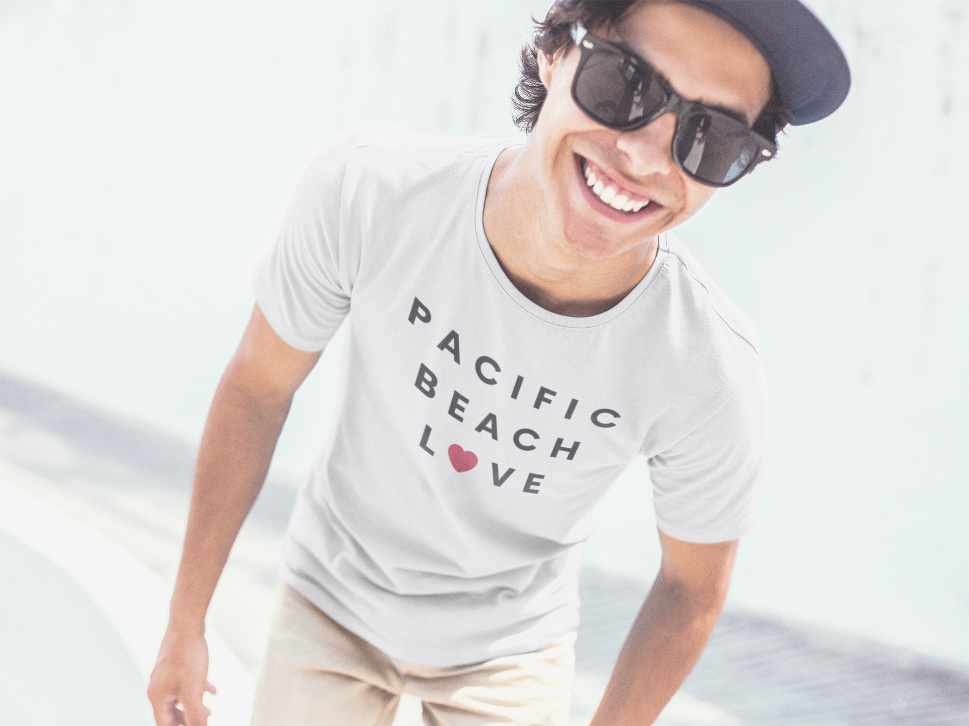 Cool guy with sunglasses and hat posing in front ocean waves. Man wearing a Pacific Beach t-shirt.