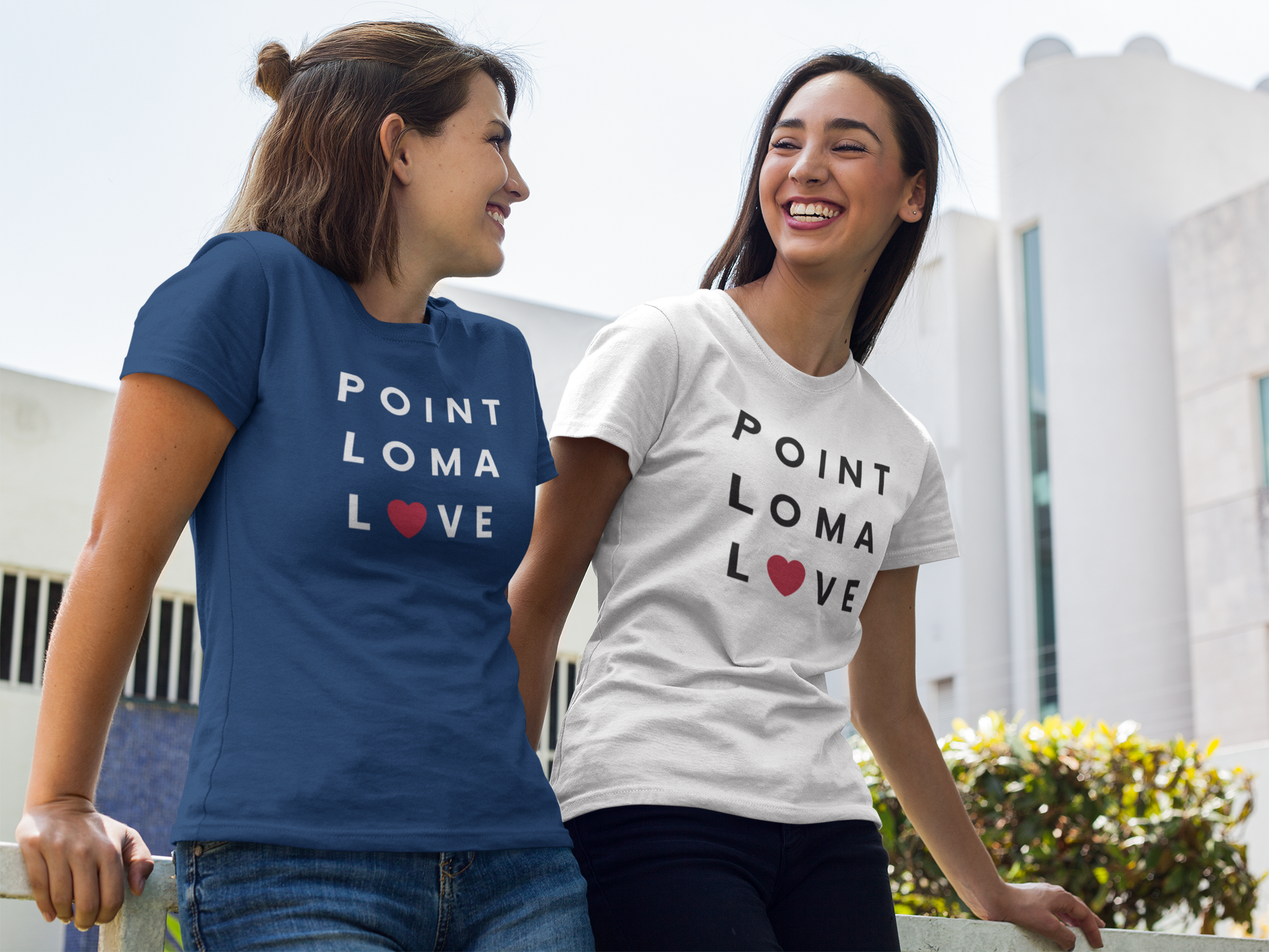 Two smiling women gazing at each other in a garden wearing Point Loma love tees.