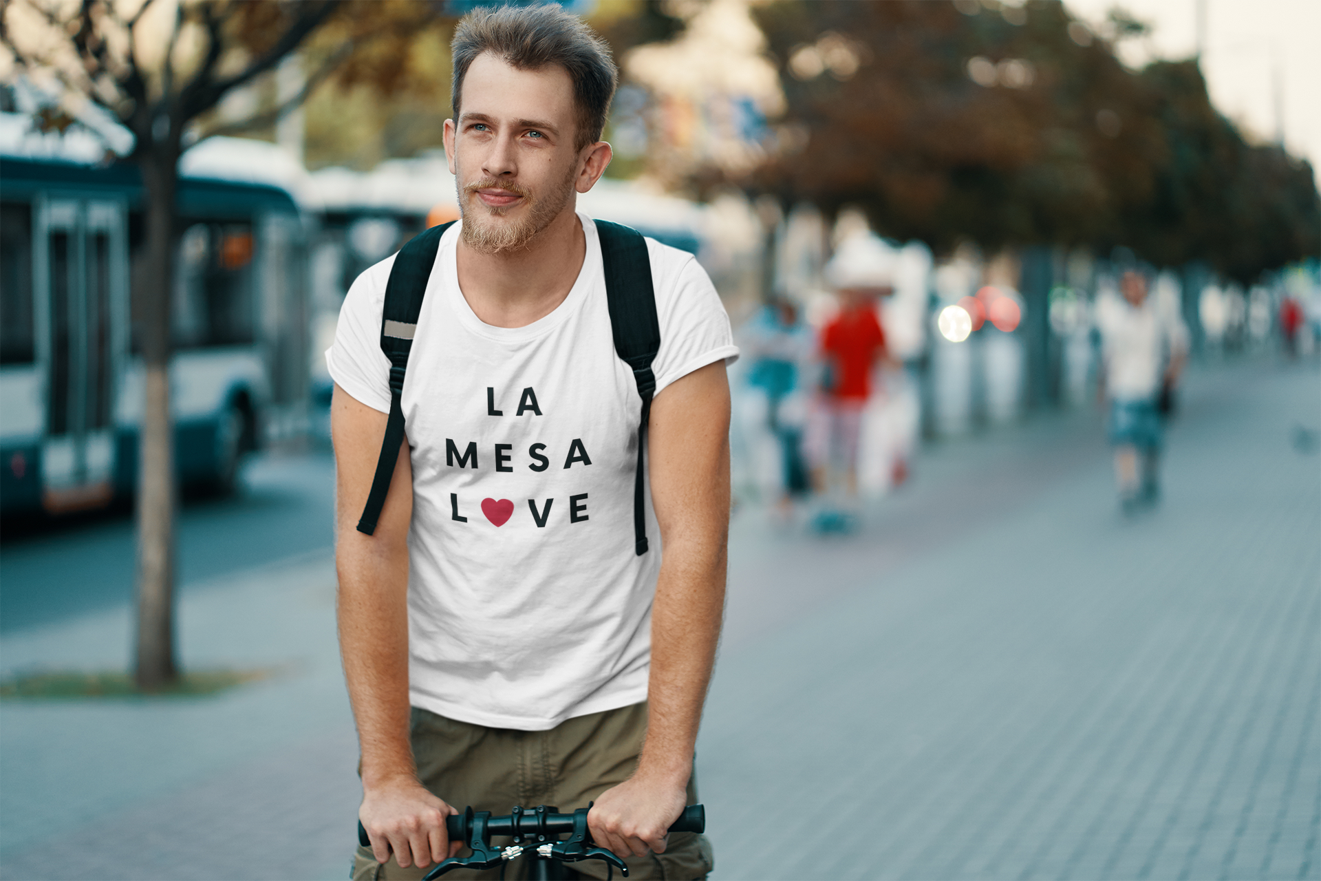 Guy riding his bike down the street wearing a back back and La Mesa t-shirt.