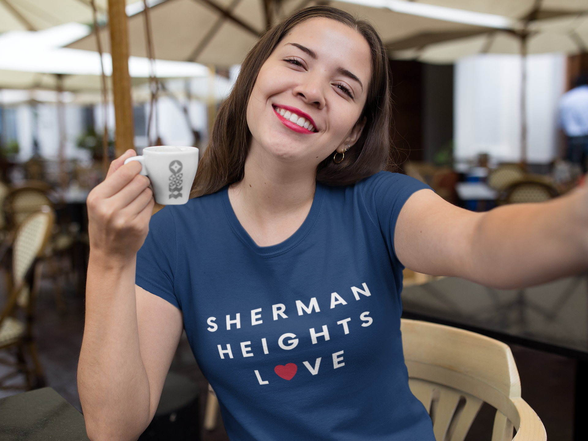 Smiling woman wearing blue Sherman Heights Love t-shirt while drinking coffee.