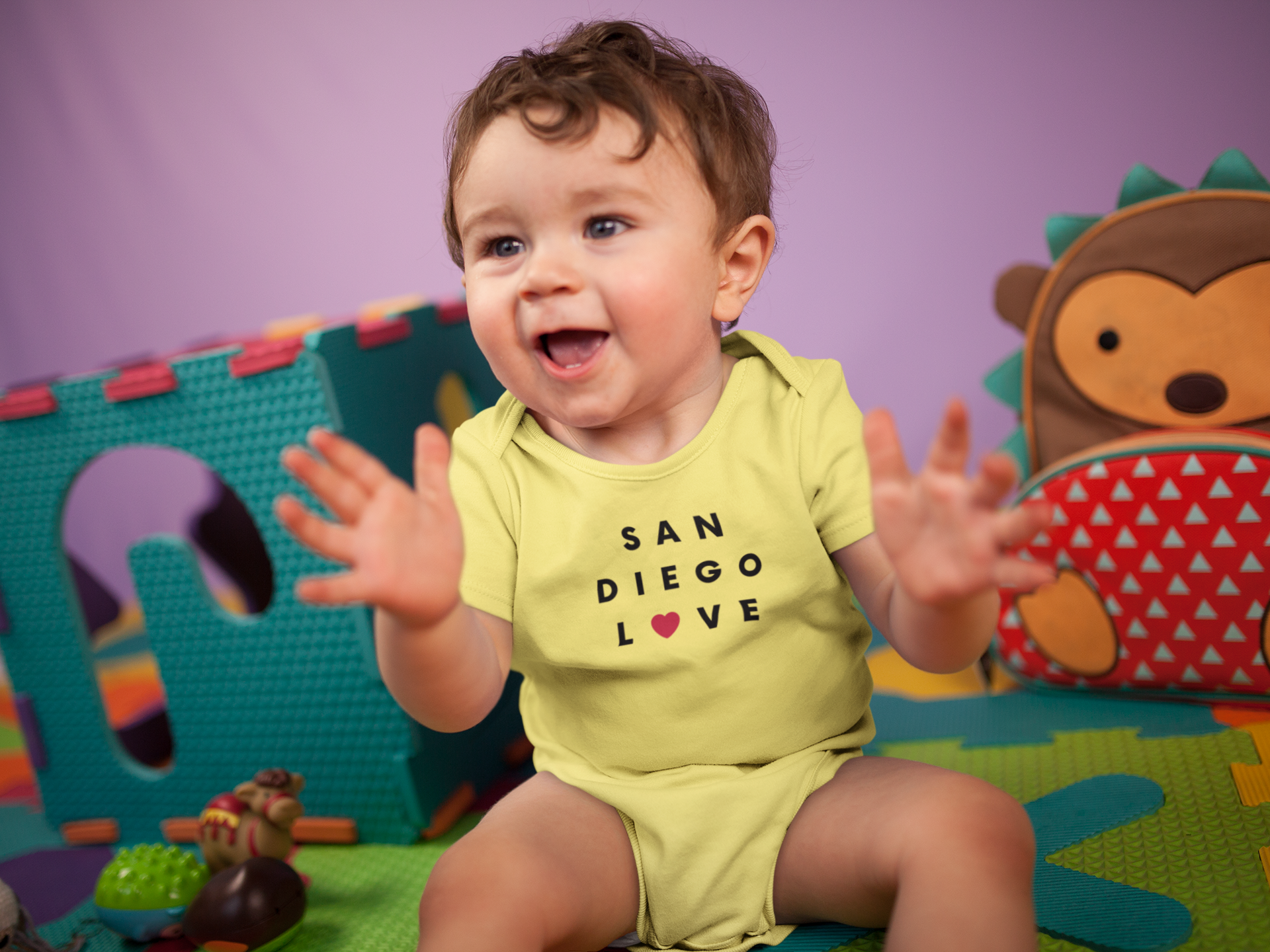 Happy baby wearing yellow San Diego Love baby onesie.