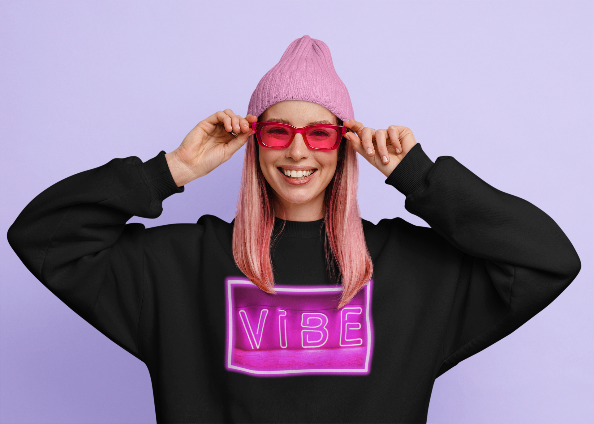 Smiling woman wearing pink beanie and sunglasses with a black and pink vibe sweatshirt.